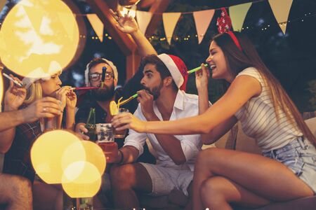 Group of young friends blowing party whistles, drinking beer, making a toast and having fun at an outdoor New Years Eve partyの写真素材