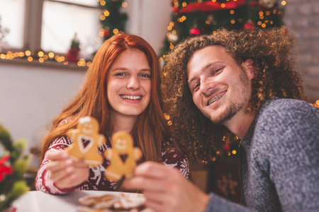 Beautiful couple in love sitting by nicely decorated Christmas tree, celebrating Christmas at home,...