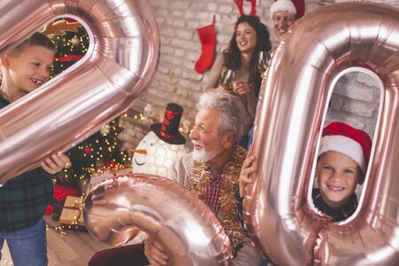 Beautiful happy family celebrating Christmas at home, having fun holding giant balloons shaped as numbers 2020, representing the upcoming New Yearの写真素材