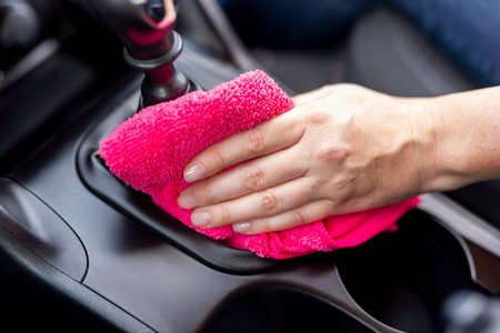 Detail of female hand wiping dust and polishing car interior parts with cleaning cloth