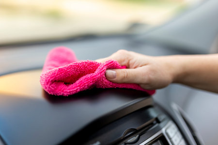 Detail of female hand wiping dust and polishing car interior parts with cleaning cloth