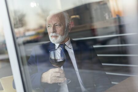 Portrait of a senior businessman sitting at a restaurant table, drinking wineの写真素材