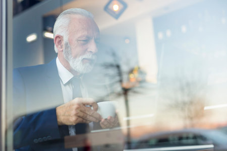 Senior businessman in a modern office working on a laptop computer and drinking coffee