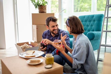 Couple in love moving in together, taking a break from unpacking cardboard boxes, having fun while...