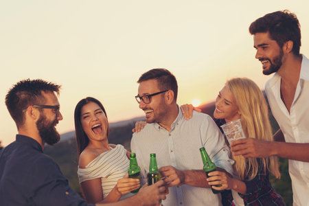Group of friends at a summertime outdoor party having fun, dancing, drinking beer and making a toast