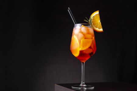 Glass of ice cold orange spritz cocktail served in a wine glass, decorated with slices of orange and rosemary branch, placed on a bar counterの写真素材