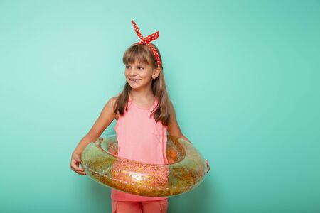 Little girl holding an inflatable swim ring, getting ready for beach summer vacation, isolated on mint colored backgroundの写真素材