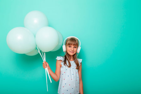Portrait of a beautiful little girl holding bunch of balloons wearing headset and listening to the...