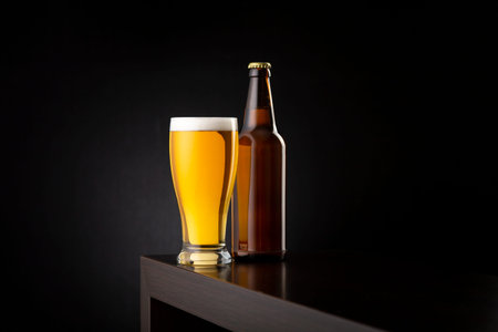 Glass of cold pale beer and a beer bottle placed on a bar counter with copy space