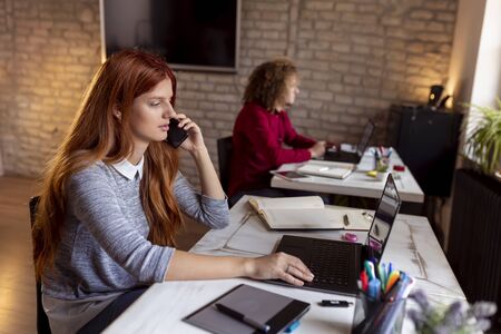 Colleagues working in a modern office; woman having a phone conversation while working in a modern coworking spaceの写真素材