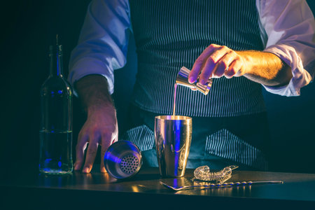 Bartender making a cocktail, pouring the ingredients from a measuring cup into a cocktail shaker