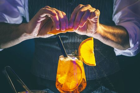 Bartender finishing up cocktail, sprinkling a cocktail wineglass with fresh orange juice to add the flavor and scentの写真素材