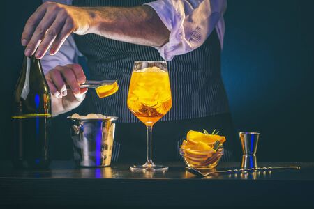 Bartender decorating cocktail, adding a slice of orange into a wineglass filled with iceの写真素材