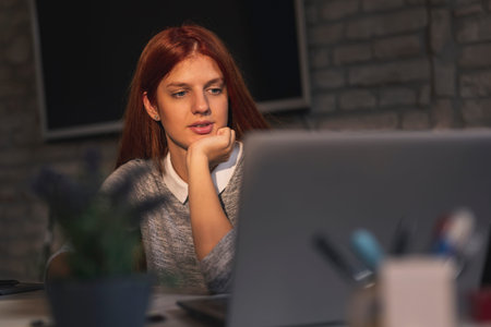 Woman telecommuting, working on a laptop computer; female freelancer working in a home office; woman...