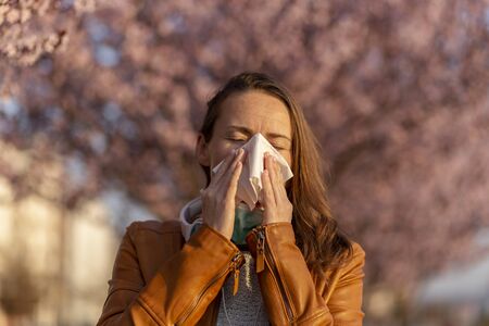 Portrait of a young woman sneezing and blowing nose outdoor, having trouble with spring pollen allergies and inhaler allergensの写真素材