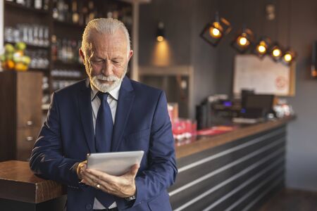 Senior restaurant manager standing next to a counter, using a tablet computerの写真素材