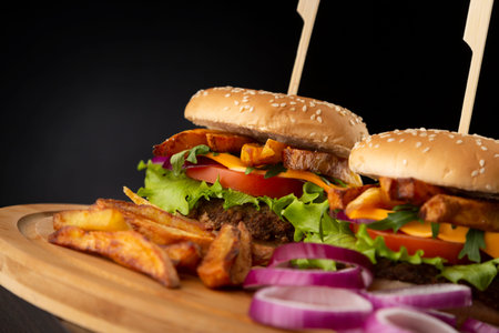 Delicious juicy fresh burgers served on a wooden tray with onions and french fries aside