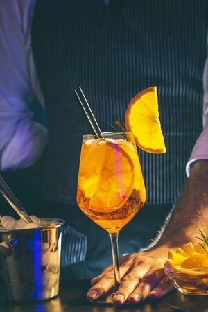 Bartender making cocktail; barman serving orange liqueur cocktail in a wineglass on a bar counterの写真素材