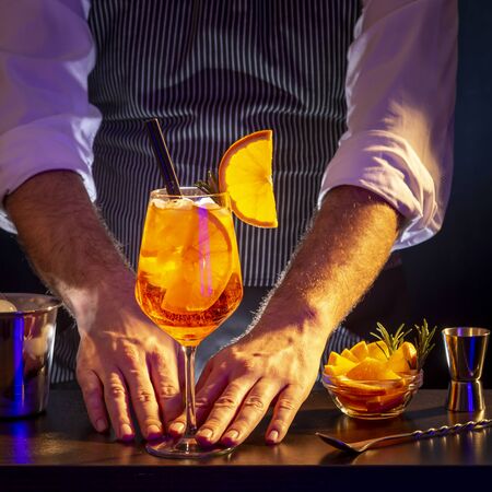 Bartender making cocktail; barman serving orange liqueur cocktail in a wineglass on a bar counterの写真素材
