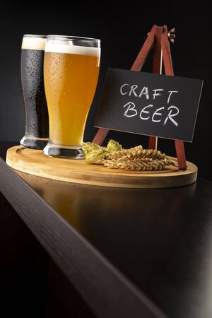 Two types of craft beer served in glasses on a bar counter; glasses of cold unfiltered wheat beer and dark beerの写真素材