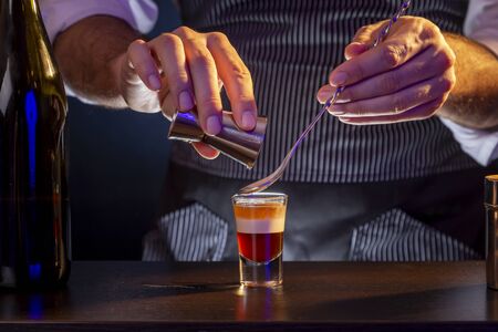 Bartender making B-52 layered cocktail, pouring irish cream from a measuring cup into a shot glass using cocktail spoonの写真素材