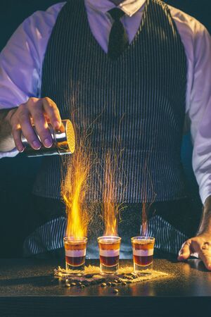 Bartender sprinkling cinnamon powder over burning layered B52 cocktails while working in a nightclub causing beautiful sparkling effectの写真素材