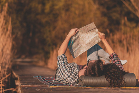Beautiful young couple in love lying on a picninc blanket at lake docks, reading a map and having...