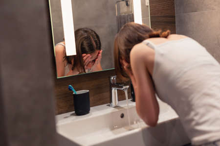 Beautiful young couple in love wearing pajamas, standing in front of bathroom mirror next to a sink, making funny faces and having fun before bedtimeの写真素材