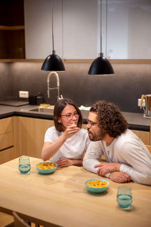 High angle view of couple in love wearing pajamas, sitting at kitchen table and having fun while eating dinner at home, relaxing at nightの写真素材