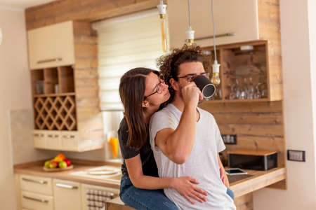 Couple in love relaxing at home in the morning, drinking coffee and hugging in kitchenの写真素材