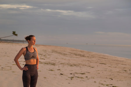 Young woman working out on the beach early in the morning, practising yoga, doing stretching out...