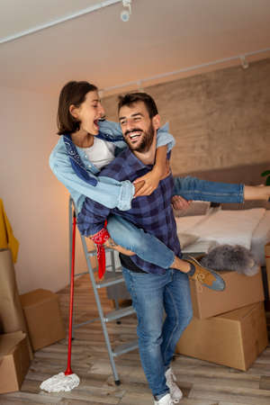 Young couple in love moving in together, having fun while unpacking cardboard boxes with their belongings, dancing in their new homeの写真素材