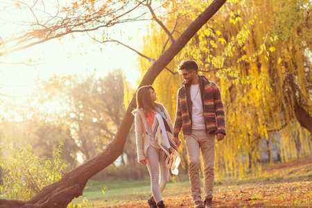 Beautiful young couple in love leaning on a tree in the park, hugging and enjoying sunny autumn day in natureの写真素材