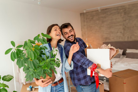 Beautiful young couple in love moving in together, having fun while unpacking cardboard boxes with...