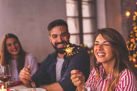 Group of friends having fun at Christmas dinner, waving with sparklers and singing Christmas songsの写真素材