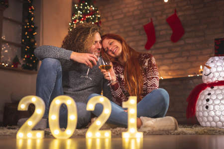 Young couple in love having fun while celebrating Christmas at home, playing the guitar, singing Christmas songs and drinking wineの写真素材