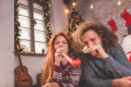 Young couple in love having fun while celebrating Christmas at home, playing the guitar, singing Christmas songs and drinking wineの写真素材