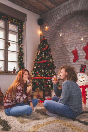 Young couple in love having fun while celebrating Christmas at home, playing the guitar, singing Christmas songs and drinking wineの写真素材