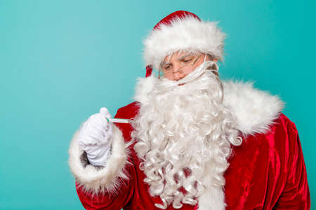 Santa Claus having fun wearing a headset, listening to the music and singing karaoke on balloon mike isolated on mint colored backgroundの写真素材