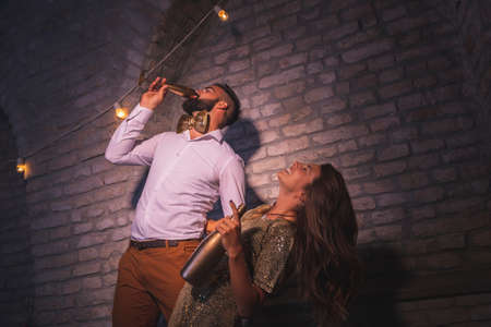 Young couple having fun at New Year's Eve party, singing, dancing and drinking champagne at midnight countdown; couple partying and drinking in nightclubの写真素材