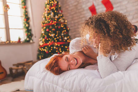 Young couple in love wearing pajamas lying in bed upside down with legs up on Christmas morning, cuddling and enjoying leisure time at homeの写真素材