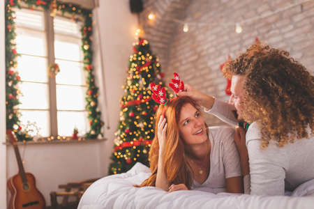 Young couple in love wearing pajamas lying in bed upside down with legs up on Christmas morning, cuddling and enjoying leisure time at homeの写真素材