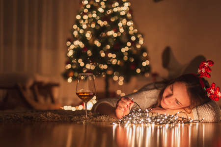Young woman enjoying leisure time at home during winter holiday season, lying on the living room floor next to a nicely decorated Christmas tree, arranging Christmas lightsの写真素材