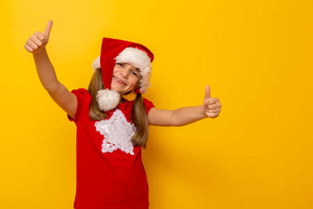 Portrait of beautiful little girl wearing deer antlers costume, holding a red cup and drinking juice, isolated on yellow colored background with copy spaceの写真素材