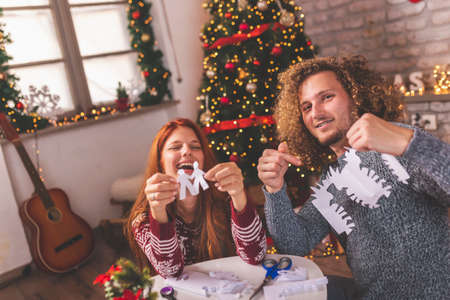 Couple in love having fun while decorating home for Christmas, setting up illuminated snowman made of plastic cups next to a Christmas treeの写真素材