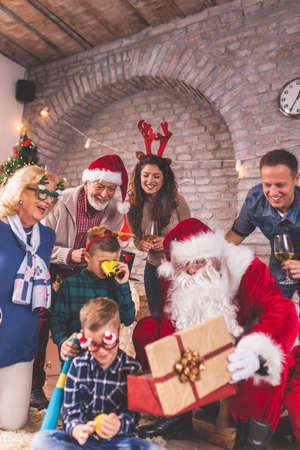 Happy family gathered at home for Christmas, having fun while opening presents with Santa Claus, children palying with their new toysの写真素材