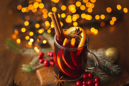 Detail of two glasses of hot red mulled wine with spices, orange slices, cinnamon stick and anise star with Christmas lights in the backgroundの写真素材