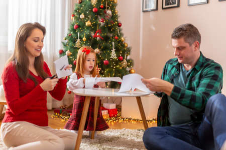 Mother, father and daughter cutting out paper snowflakes and having fun while making Christmas decorations at homeの写真素材