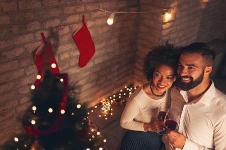High angle view of beautiful young couple in love standing by nicely decorated Christmas tree, drinking wine and enjoying spending Christmas eve together at homeの写真素材