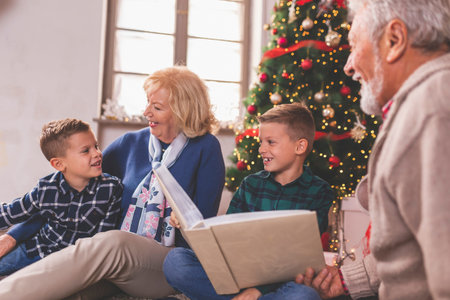 Happy family celebrating Christmas together at home, children playing with their grandparents by nicely decorated Christmas treeの写真素材